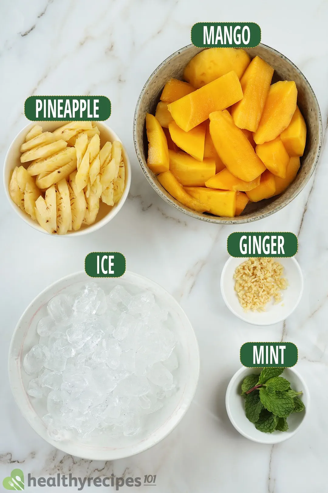 Ingredients for Mango Ginger Smoothie, including bowls of mango wedges, pineapple slices, ice, sliced ginger, and mint leaves.