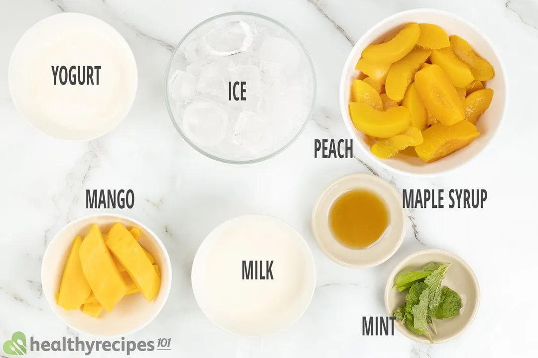Ingredients for peach smoothie, including bowls of sliced peach, sliced mangoes, mint leaves, ice, yogurt, and others.