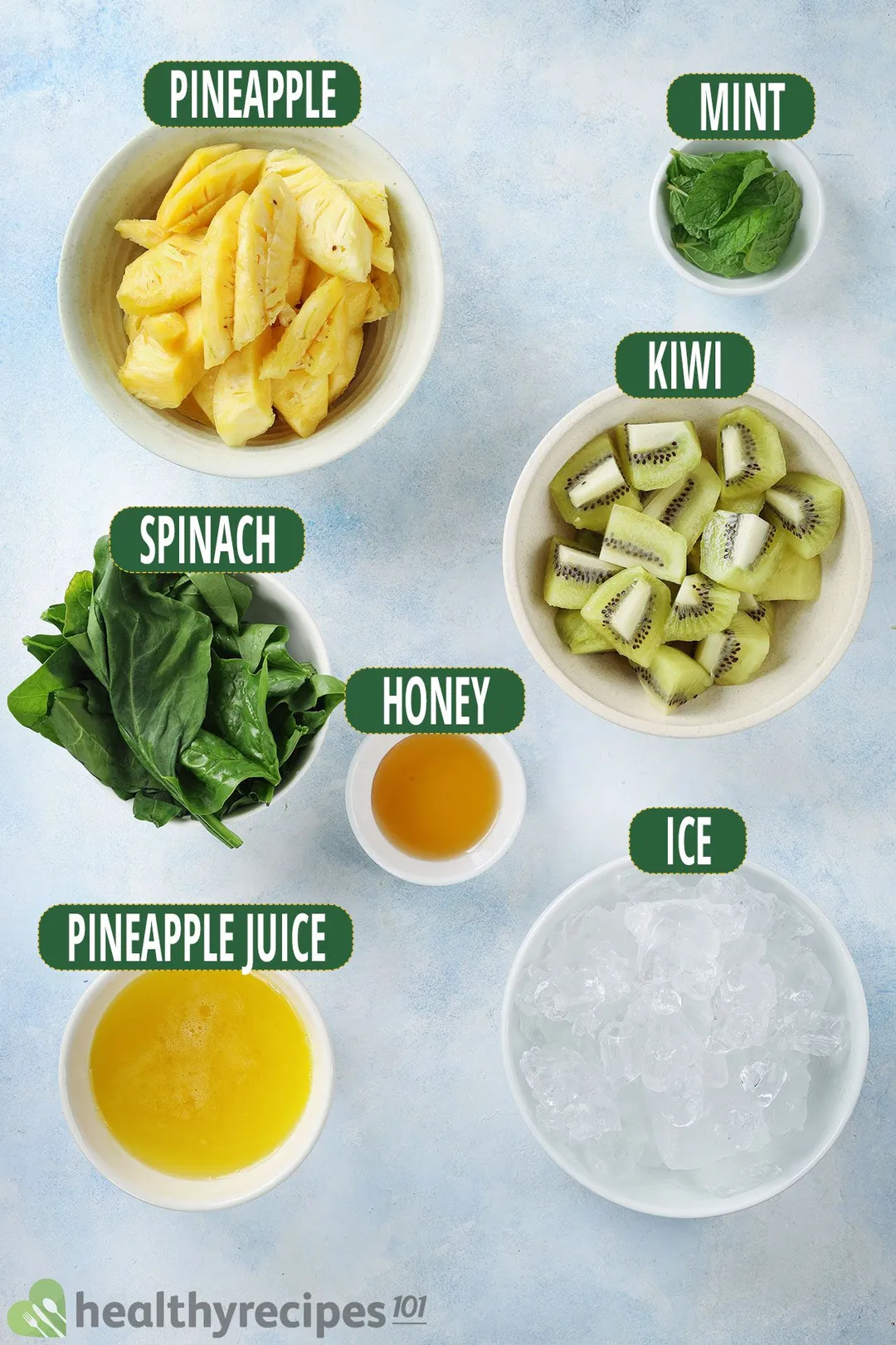 Ingredients for Pineapple Kiwi Smoothie, including bowls of pineapple slices, green kiwi slices, spinach, ice, and other smoothie essentials.