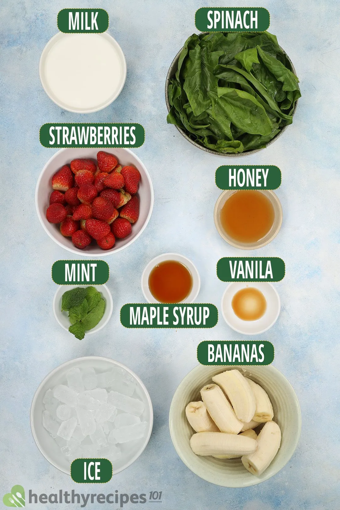 Ingredients for strawberry spinach banana smoothie, including fresh spinach, strawberries, sliced bananas, ice, honey, and other smoothie essentials.