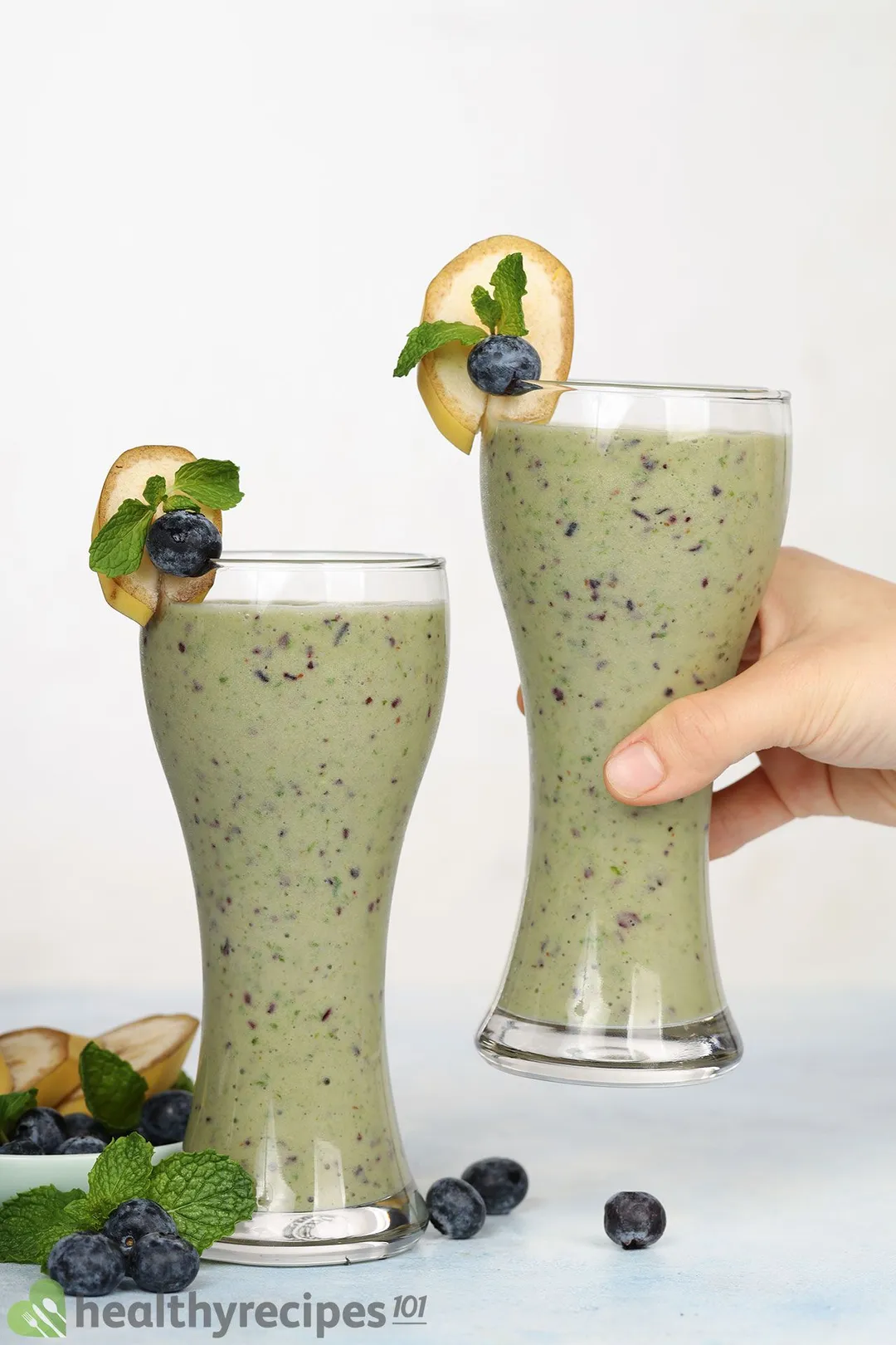 two glasses of blueberry kale smoothie, a hand holds one.