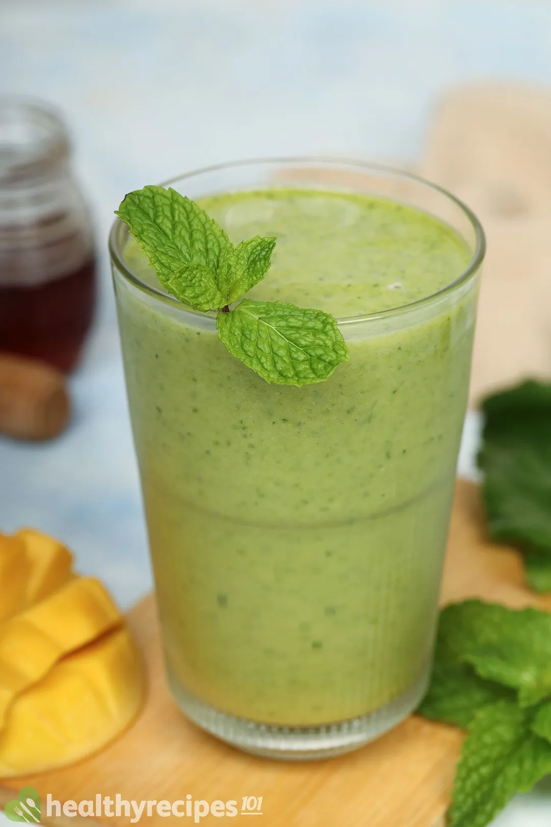 A glass of Mango Spinach Smoothie garnished with mint leaves and placed on a wooden board near a scored mango.