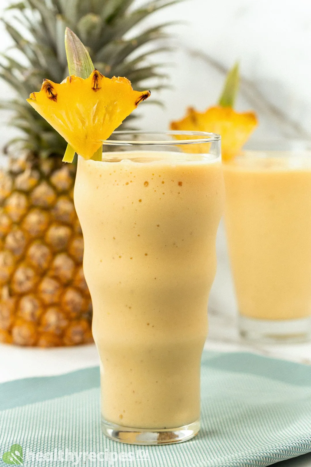 a glass of pineapple smoothie decorated with a pineapple