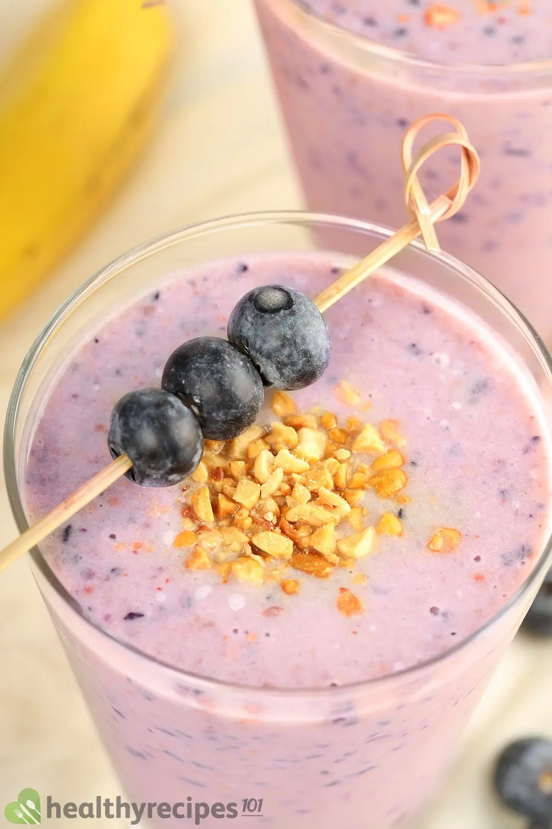 A close-up shot of a blueberry smoothie glass topped with a blueberry skewer and crushed peanuts