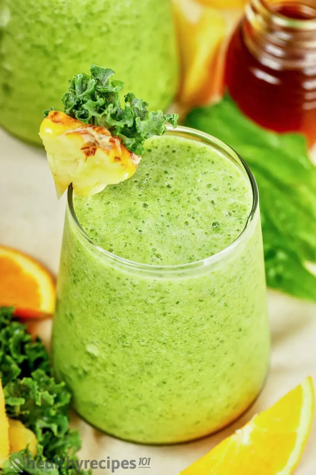 a glass of pineapple green smoothie with a pineapple wedge and kale leaves placed on its rim