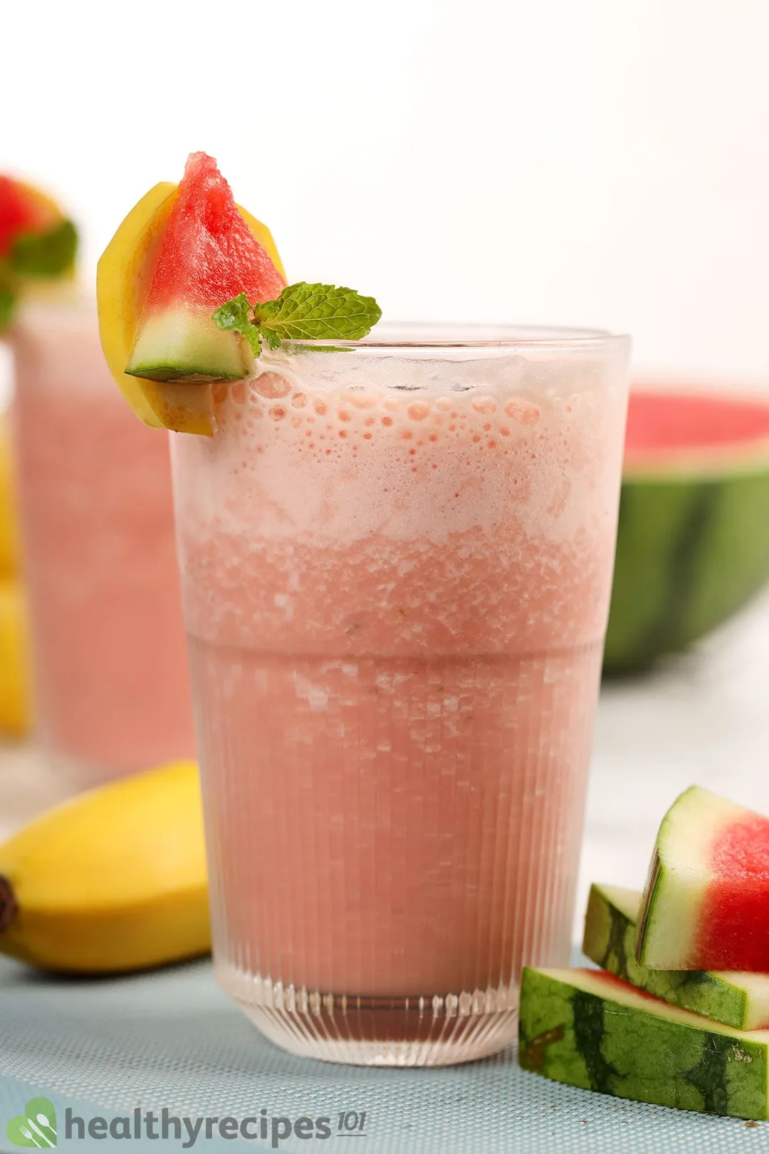 A glass of Watermelon Banana Smoothie placed near watermelon slices and a banana.