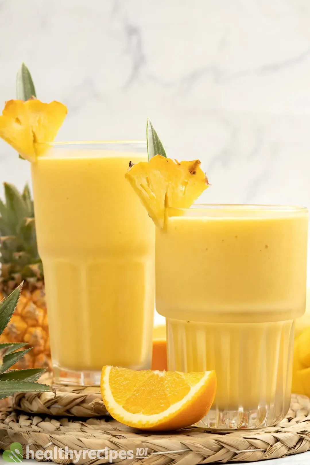 Two glasses of orange smoothies put next to each other, garnished with orange and pineapple wedges