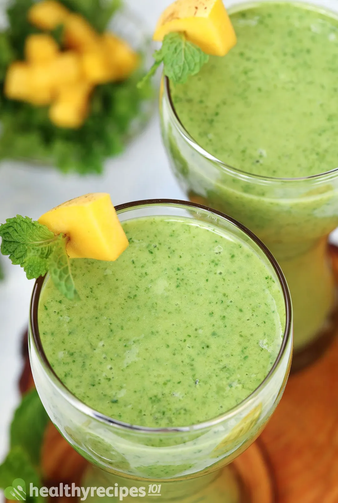 top view of two glasses of green smoothie decorated with mango cubes and mint leaves