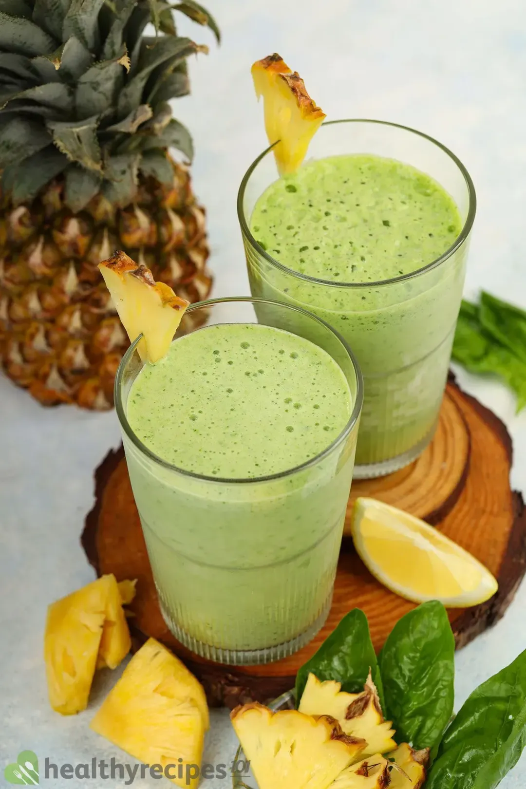 Two glasses of green smoothie put next to each other, surrounded by pineapples wedges as decoration