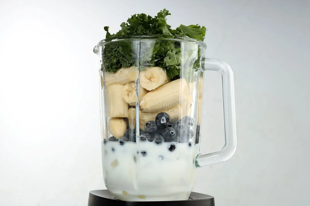 kale, banana, blueberries and milk in a blender pitcher