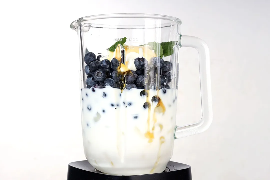 blueberries, milk, yogurt, mint and ice in a blender pitcher 