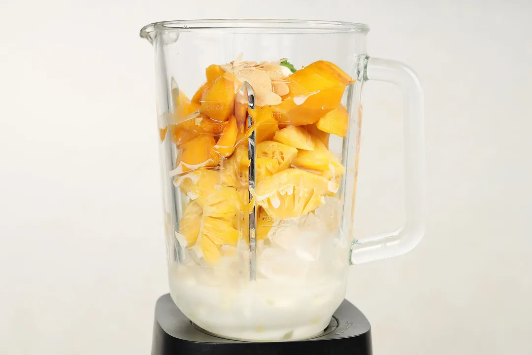 mango cubes, pineapple cubes, ice, milk and almond slices in a blender pitcher
