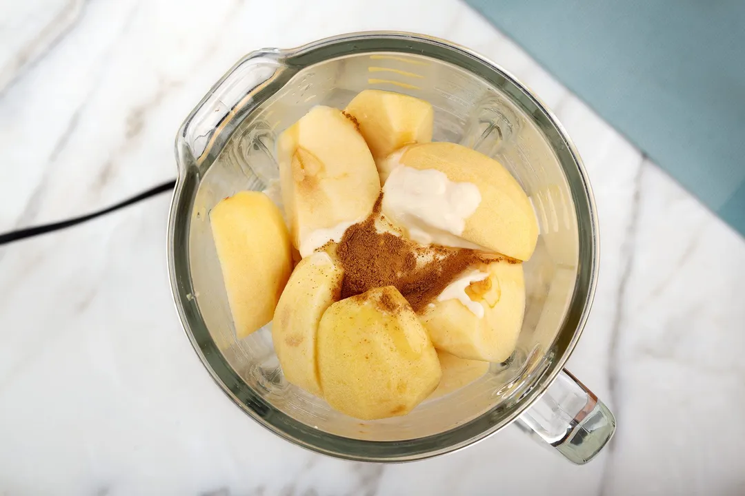 top view of a blender pitcher with apple cubed, cinnamon, yogurt in it.