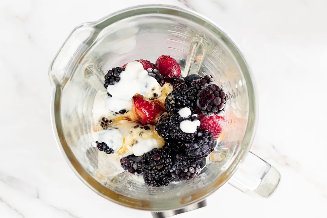 frozen blueberry, blackberry, strawberry, milk, honey in a blender pitcher