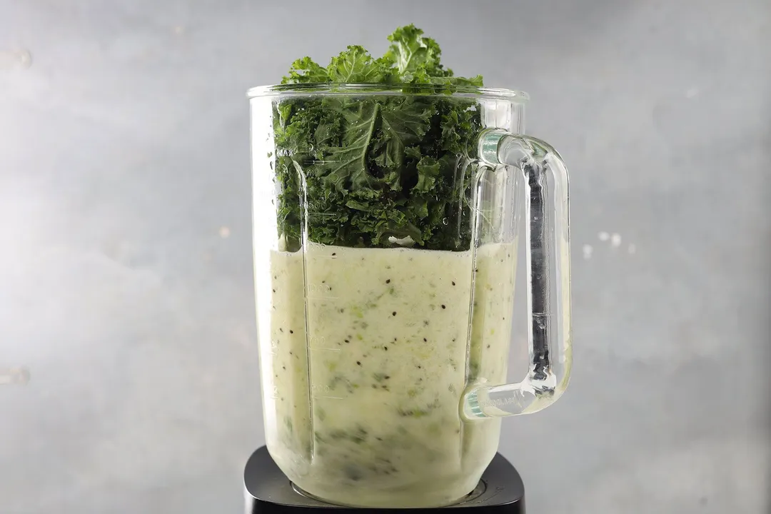 A blender filled with a green yogurt liquid and fresh kale.