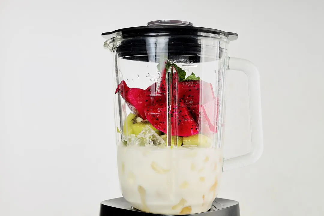 A blender filled with ice, red dragon fruit, and green kiwi.