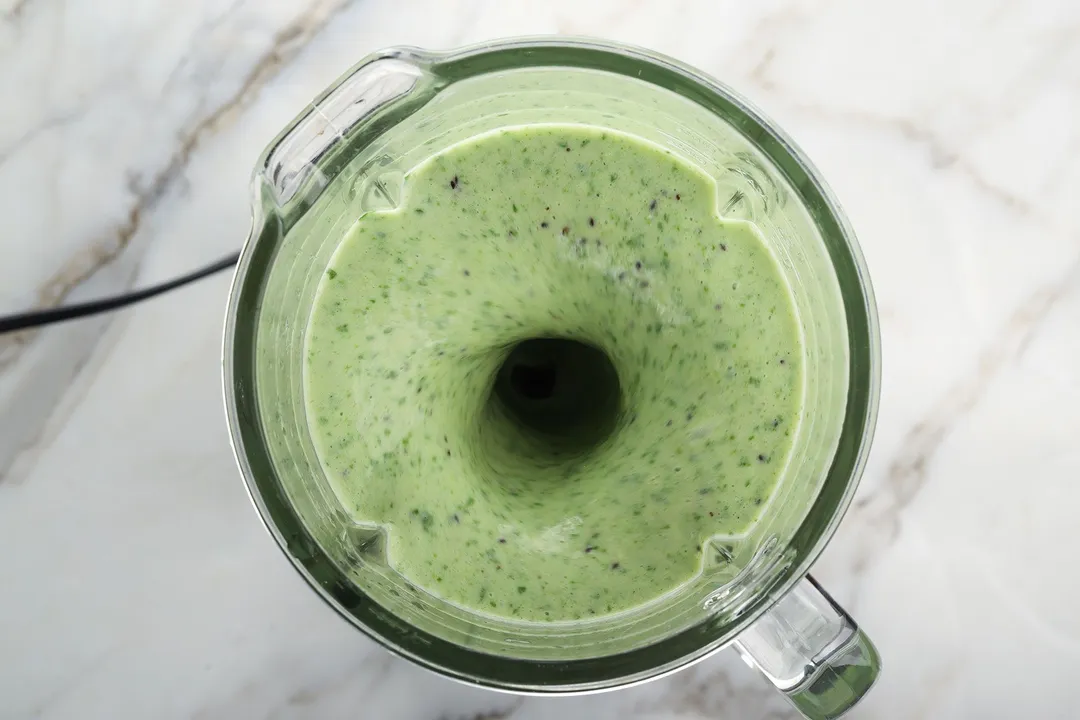 A high angle shot of a blender blending a pale green smoothie.