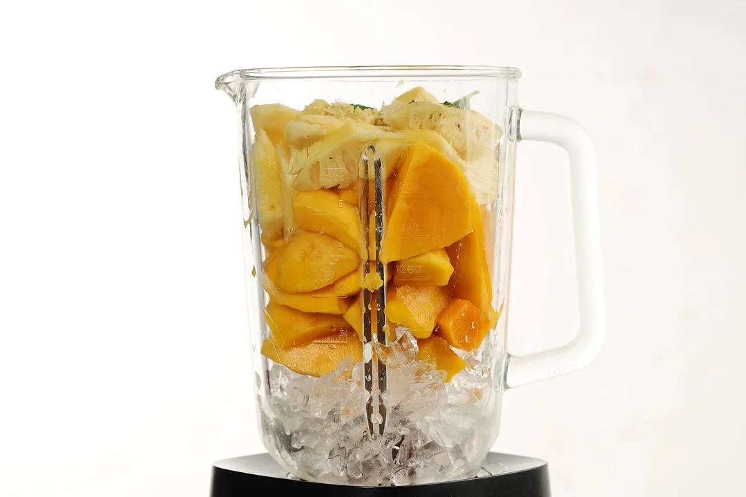 A blender filled with ice, sliced mangoes, and pineapple slices.
