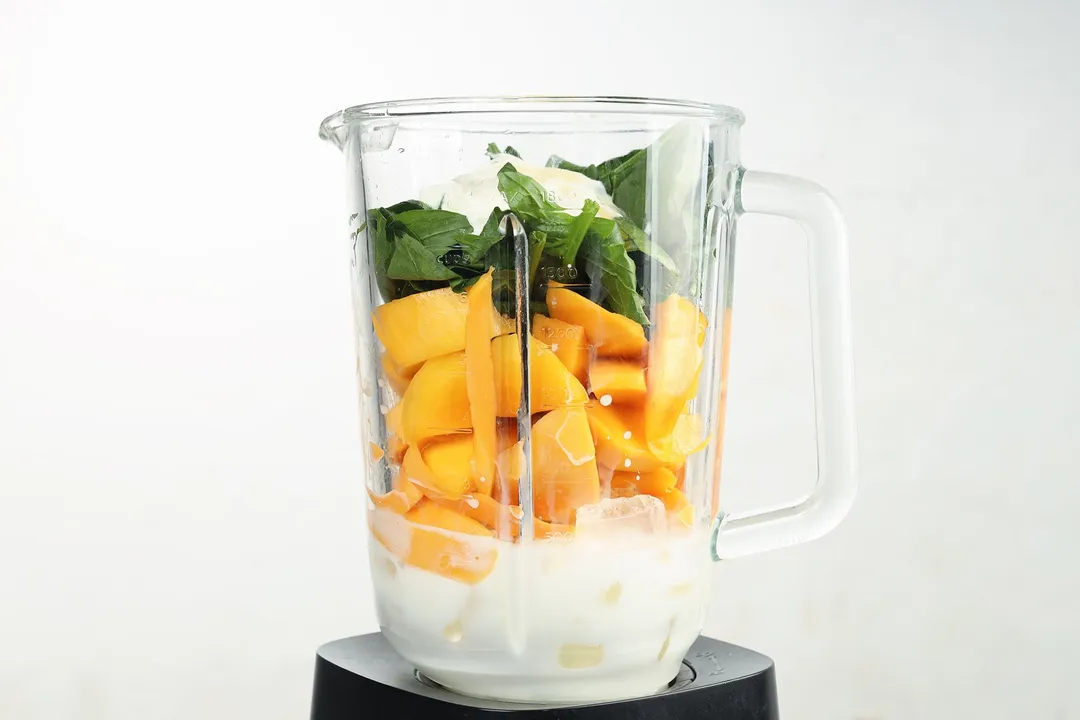 A blender filled with milk, mango wedges, and fresh spinach.