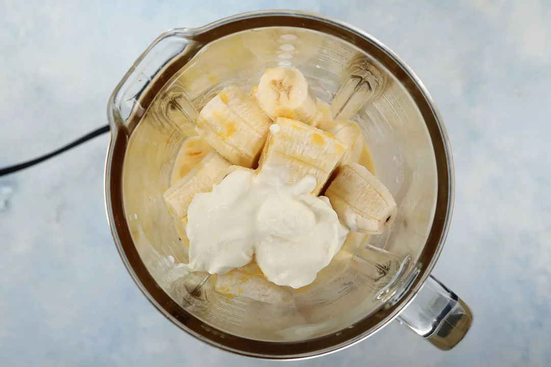 A blender filled halfway with bananas and yogurt.