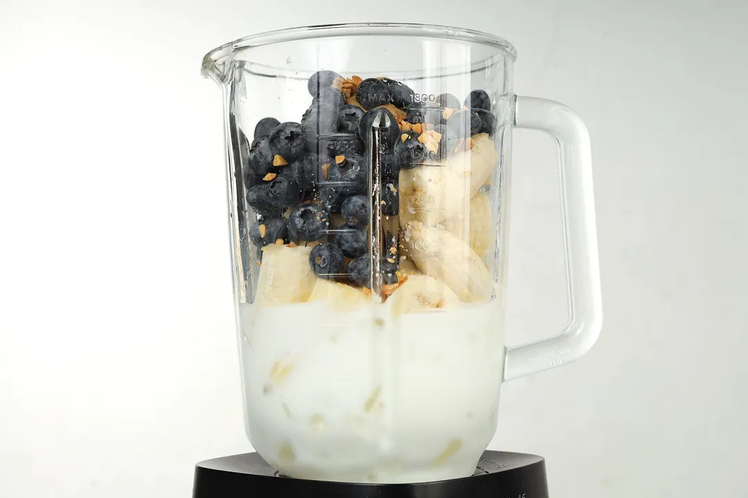 A blender filled with blueberries, bananas, and milk