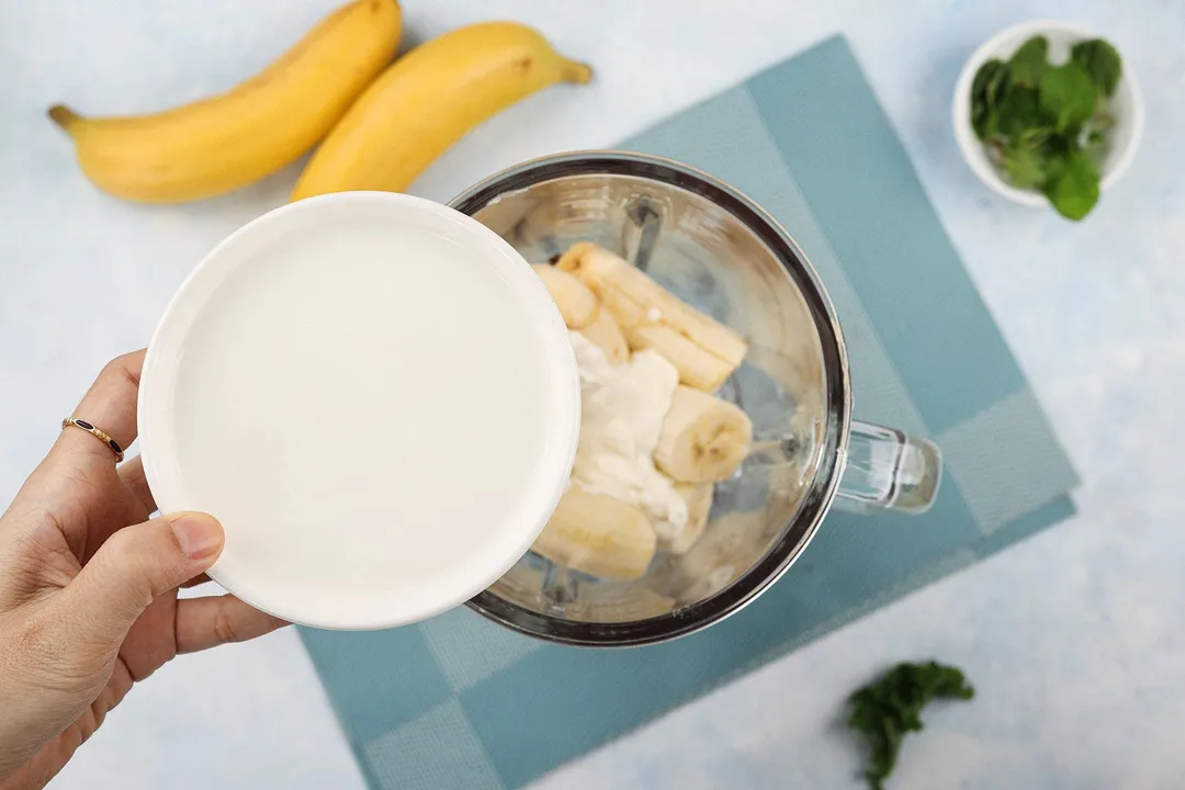 a hand holding a bowl of water pouring into blender pitcher