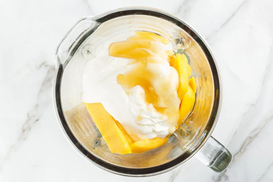mango cubed, ice and yogurt in a blender pitcher