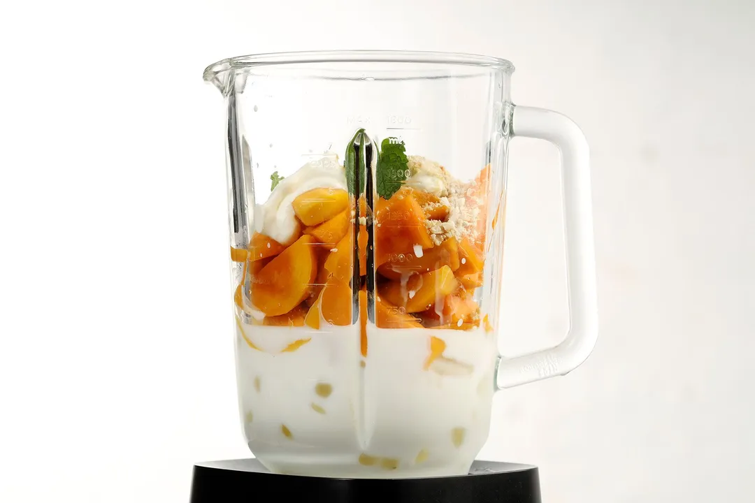 a blender pitcher of cubed mango, milk and mint leaves