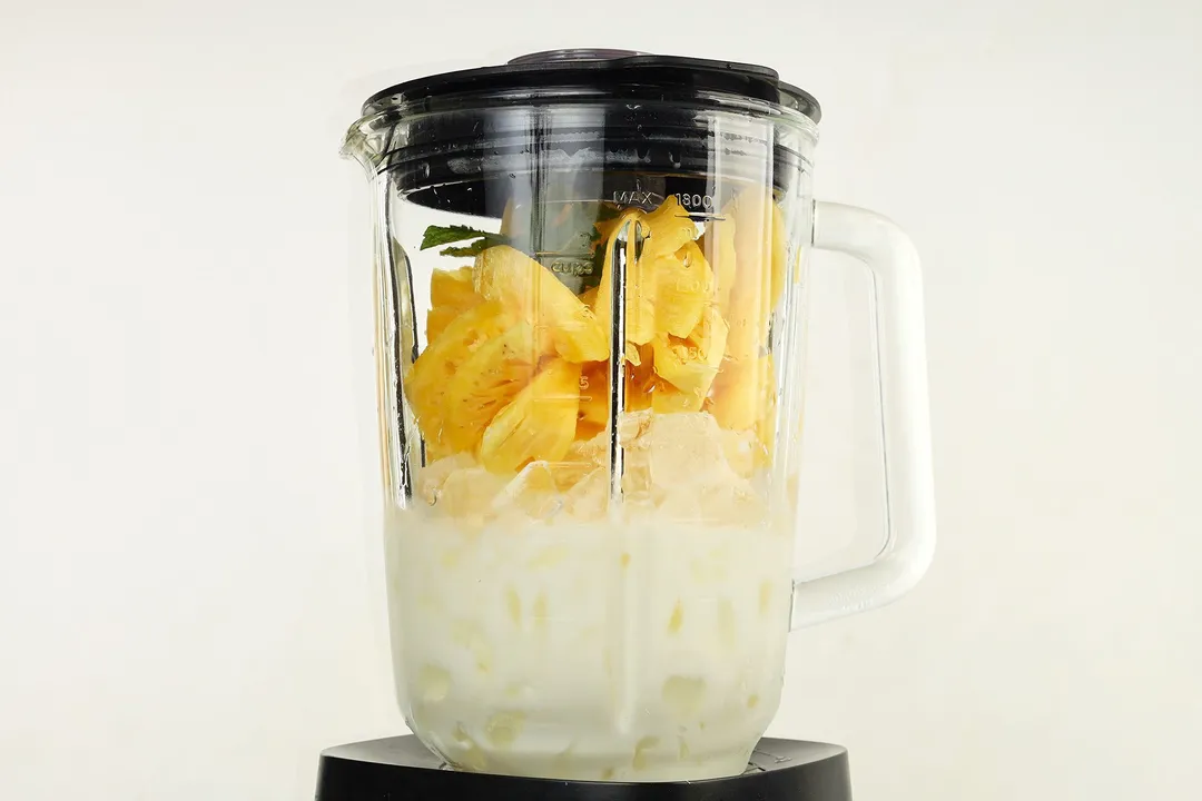 a blender pitcher with full of pineapple cubes, ice and milk in it.