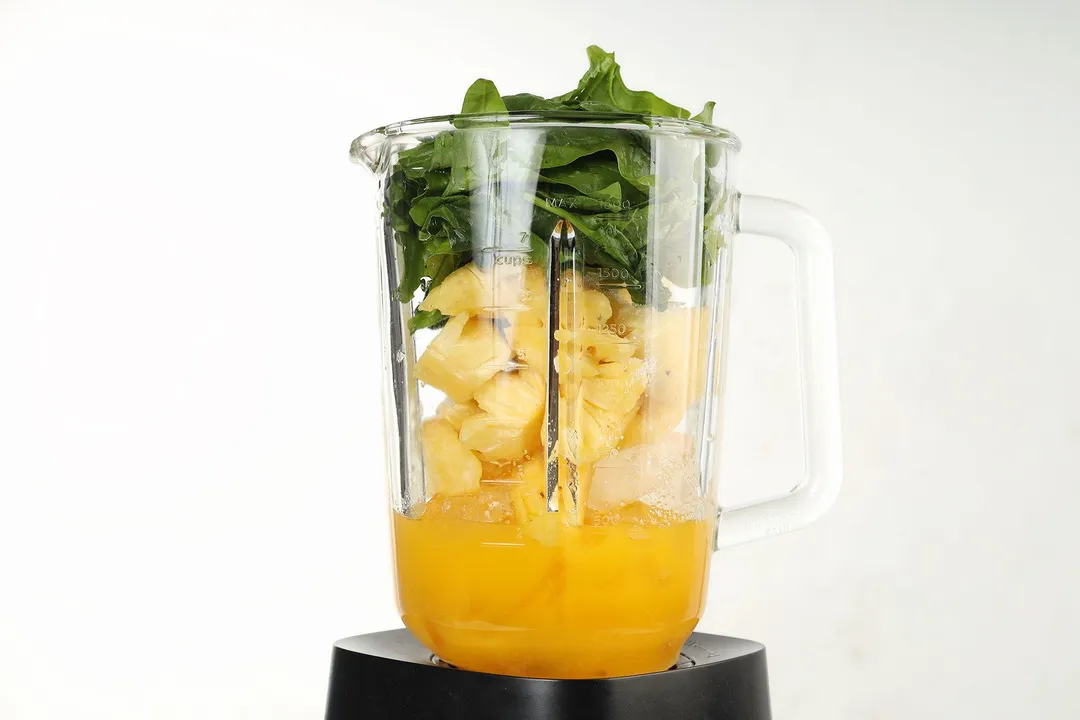 a blender pitcher of pineapple cubed and spinach