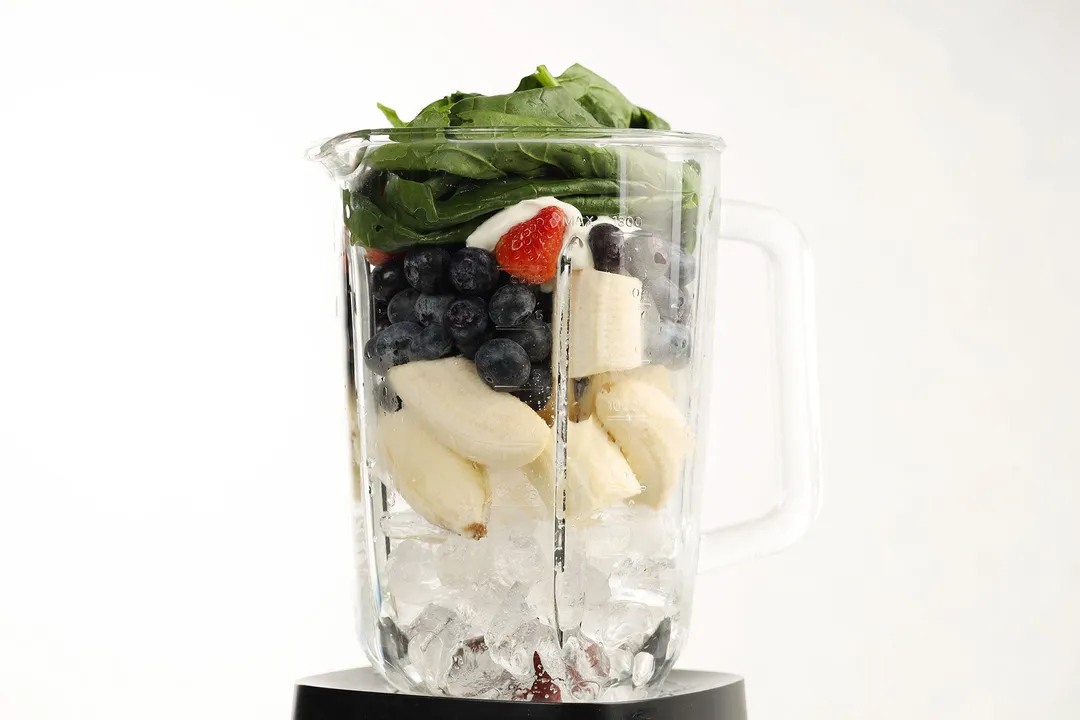 a blender pitcher of spinach, blueberries, banana, strawberries, yogurt and ice