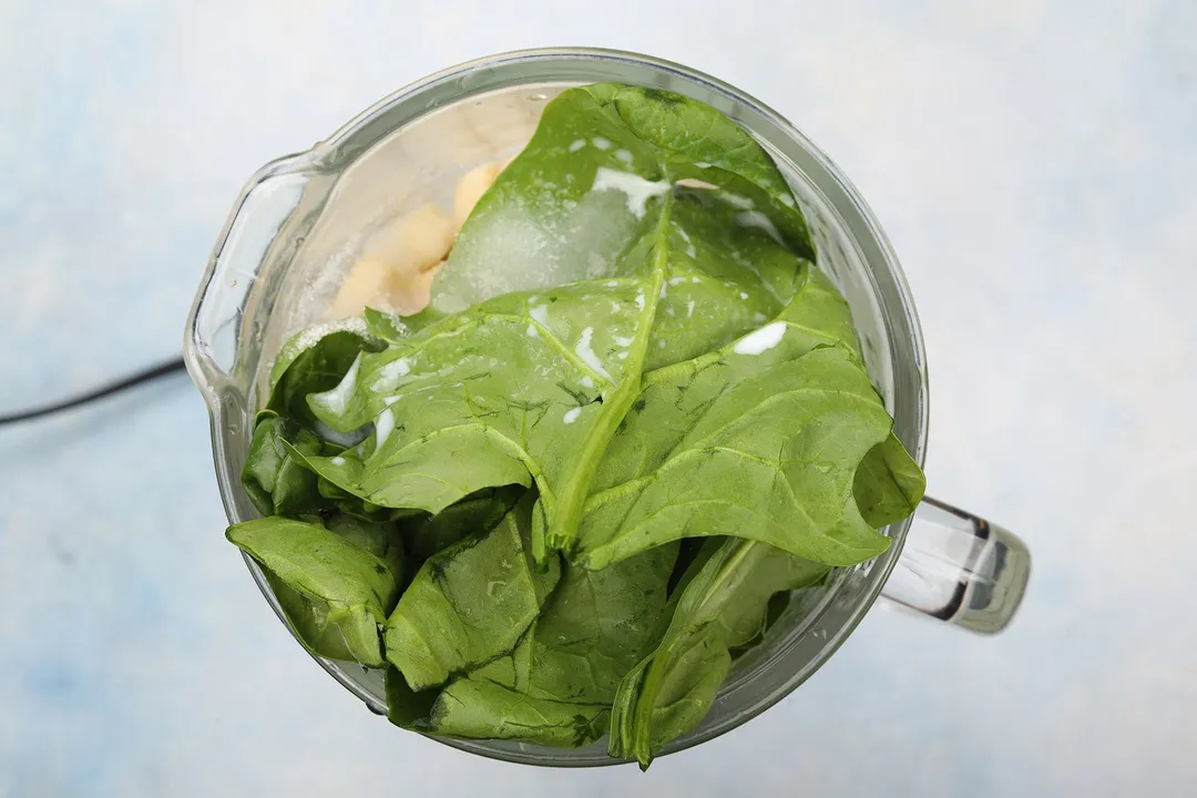 top view of a blender pitcher with spinach, banana and sugar in it