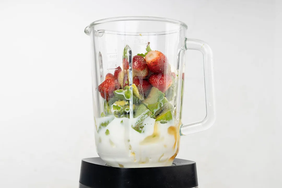 a blender pitcher of strawberry, avocado cubes milk and ice in it