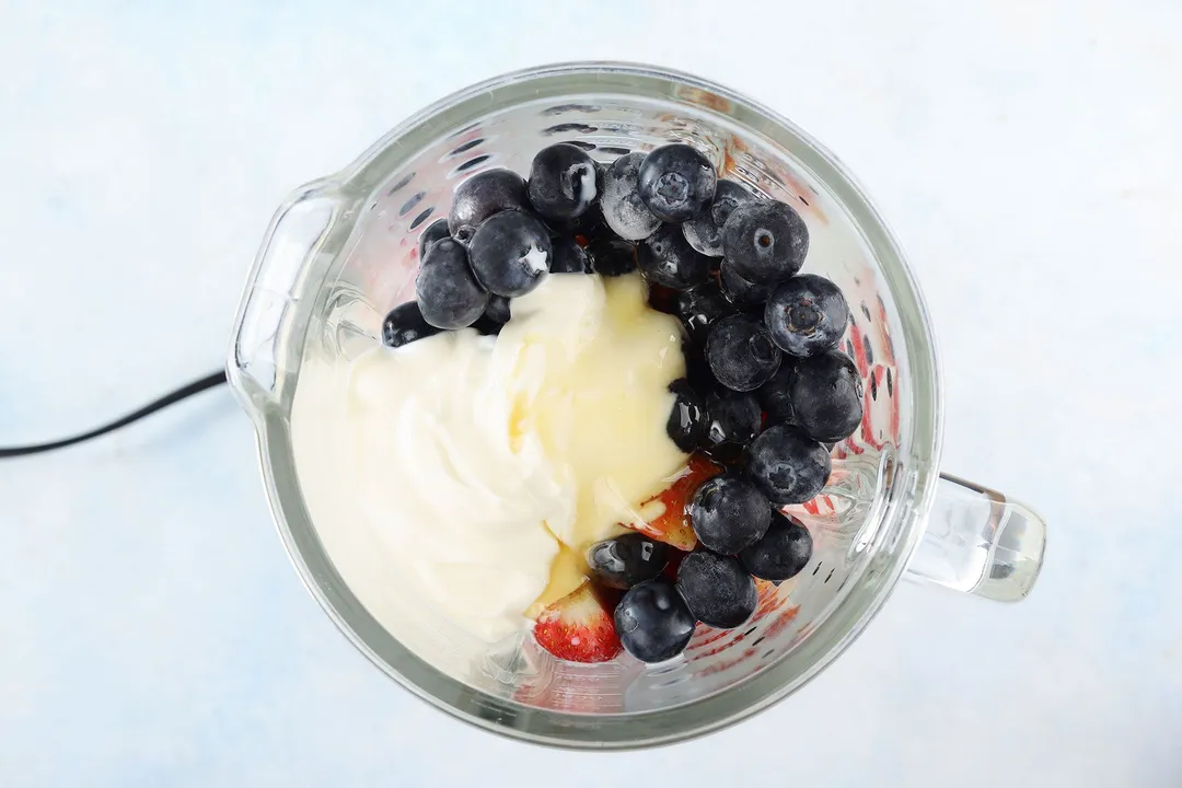 top view of a blender pitcher with blueberry, strawberry, yogurt and milk in it