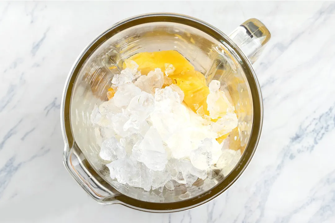 top view of a blender pitcher with ice, mango cubed and pineapple cubed in it.