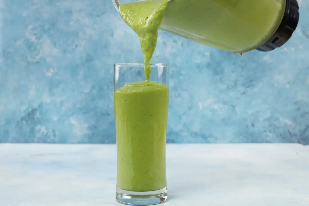 a blended avocado green smoothie poured from the blender to a glass