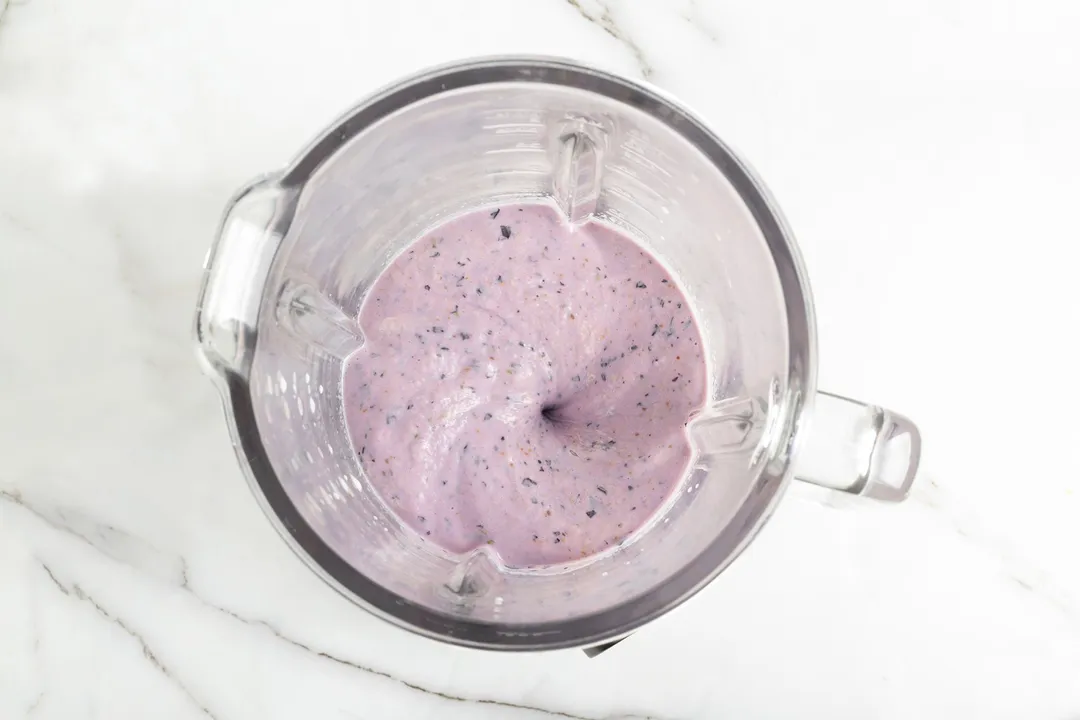 A high-angle shot of a blender filled halfway with a purple liquid that's blueberry banana smoothie.