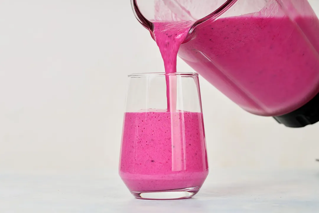 A blender pouring Dragon Fruit Smoothie into a glass.