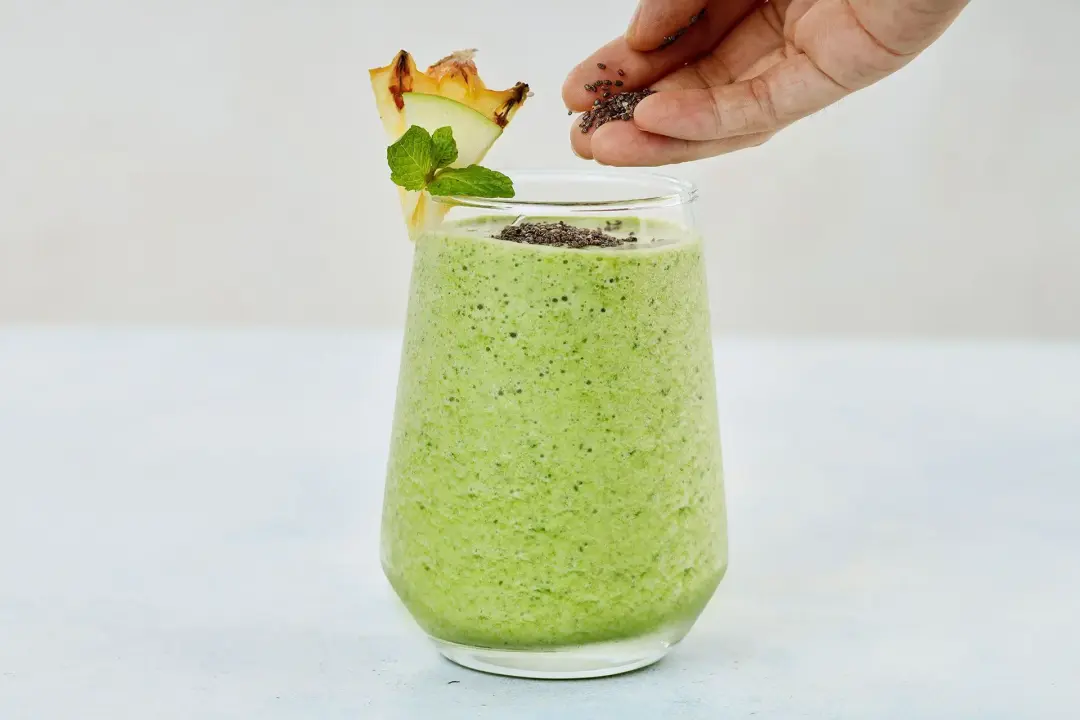 A glass of green apple smoothie being garnished with chia seeds