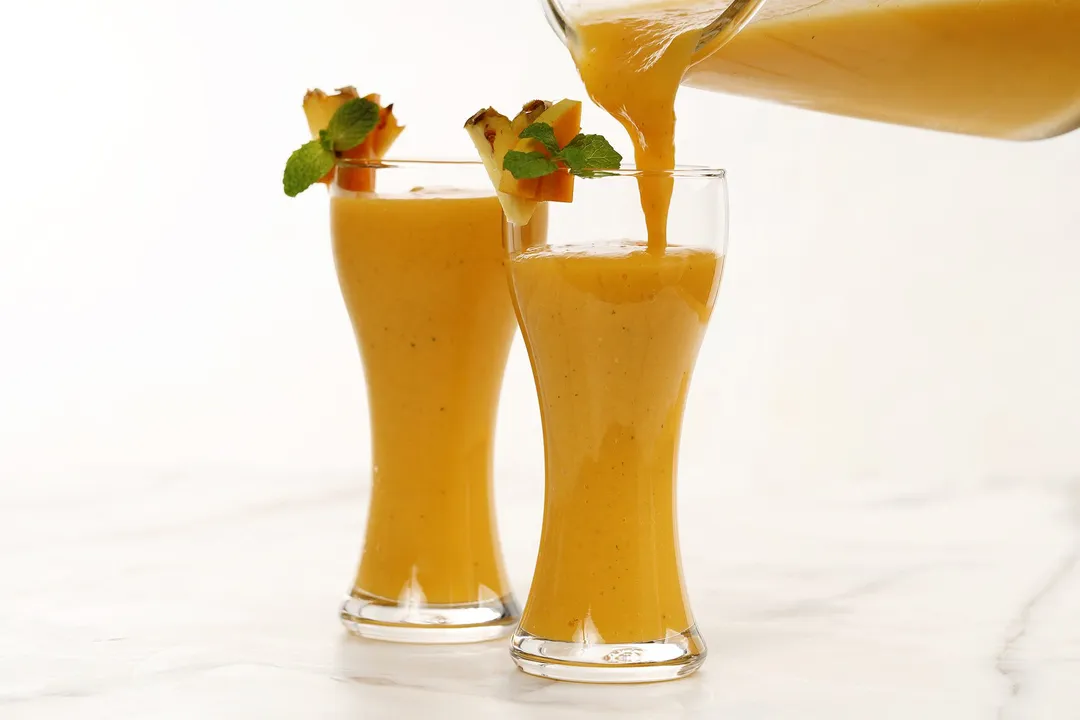 A blender pouring Mango Ginger Smoothie into two tall glasses.