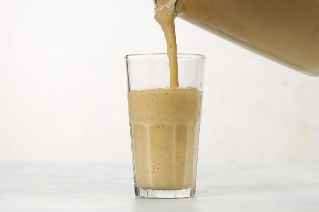 A blender pouring Orange Banana Smoothie into a glass.