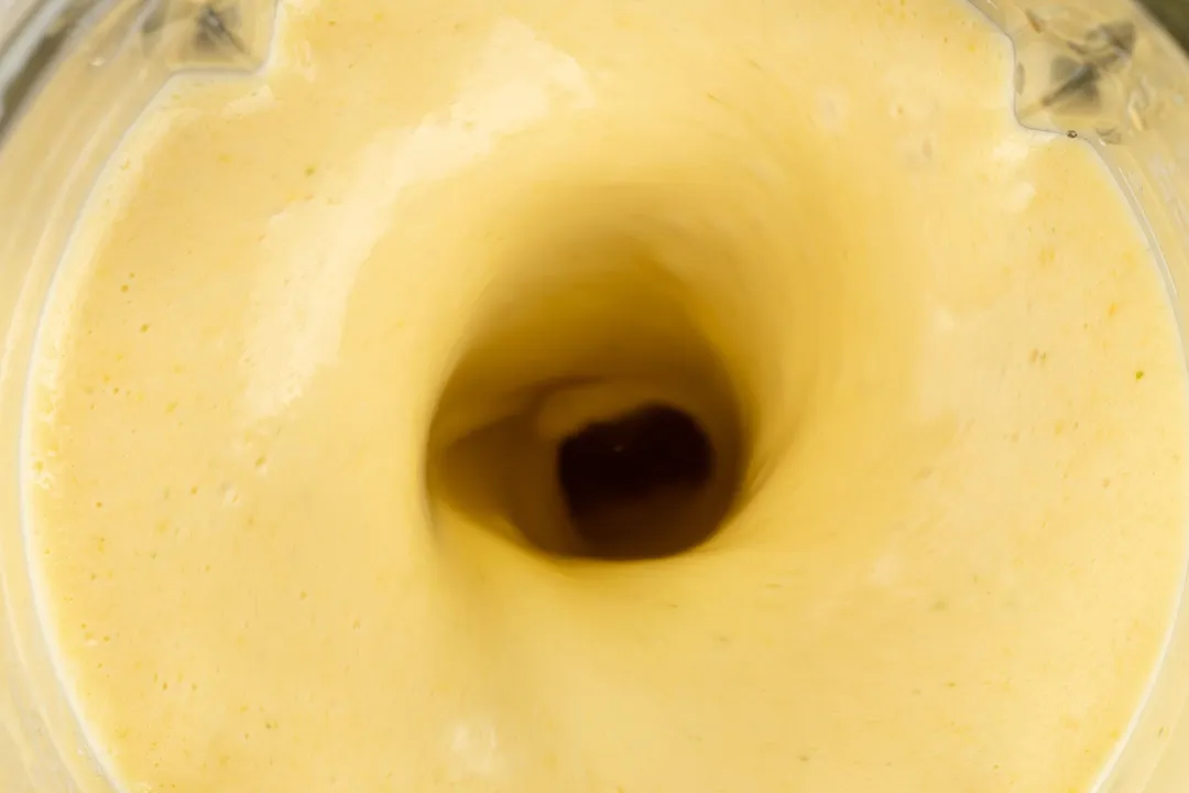 A high-angle shot of a blender creating a vortex of a thick, yellow peach smoothie.