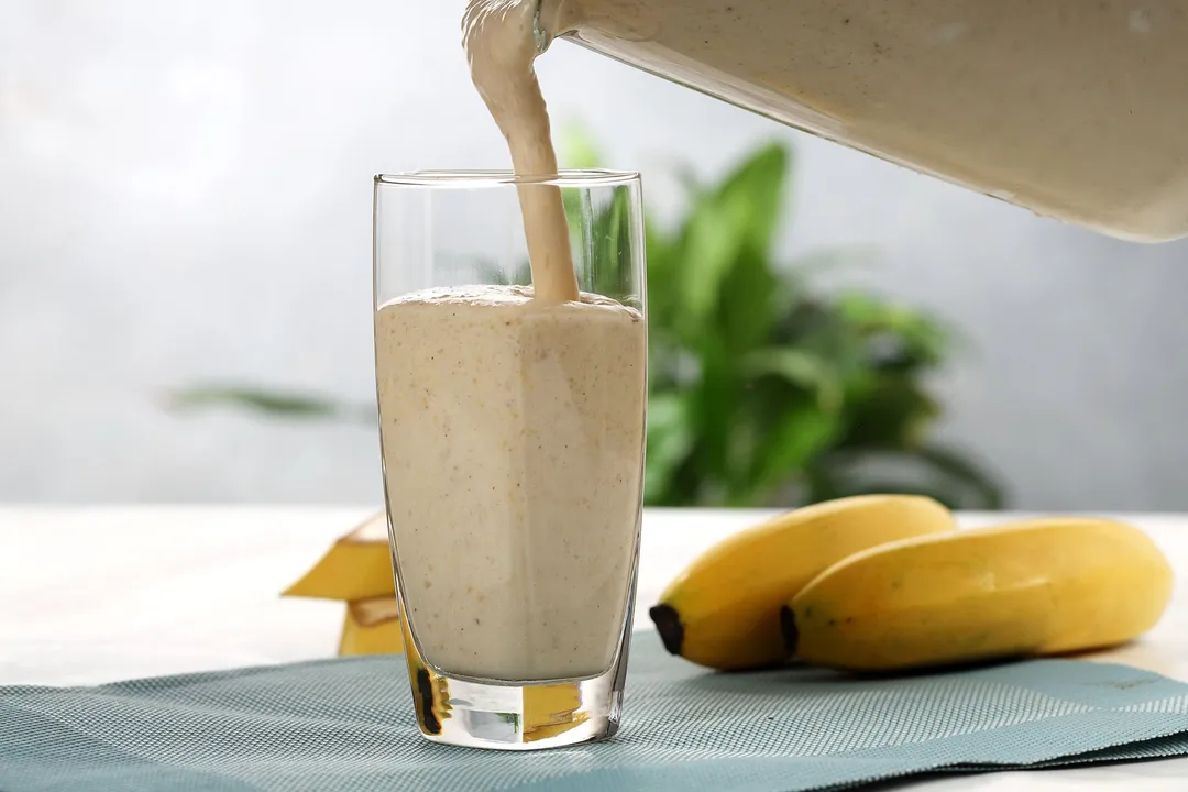A blender pouring Peanut Butter Banana Smoothie into a tall glass.