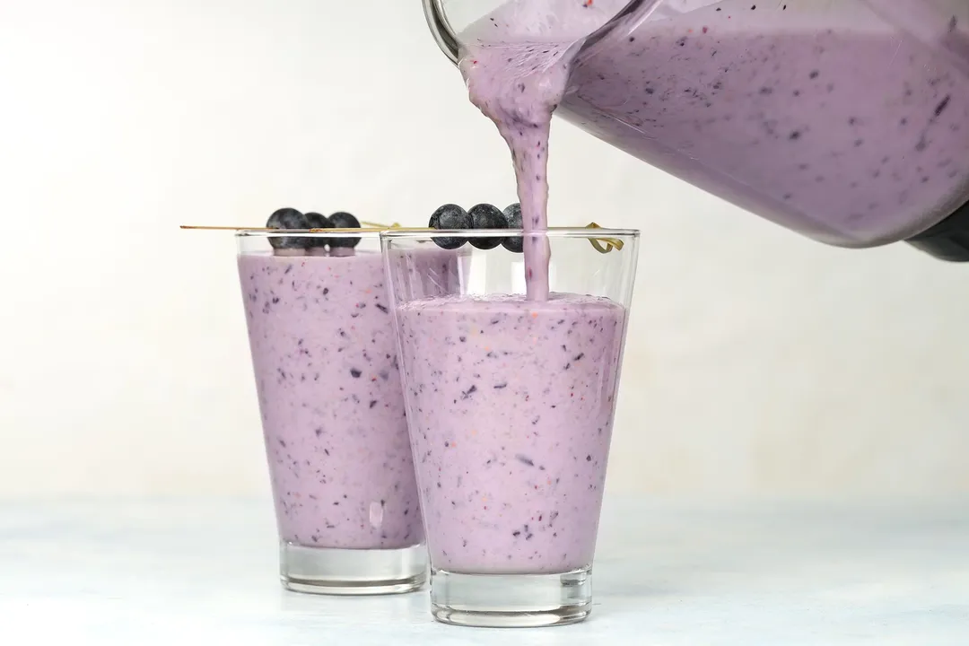 Pouring a banana blueberry smoothie into two glasses