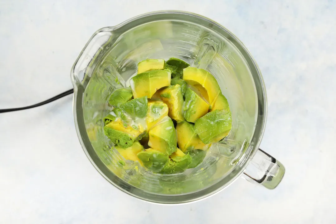 top view of a blender pitcher with cubes avocado and milk in it.