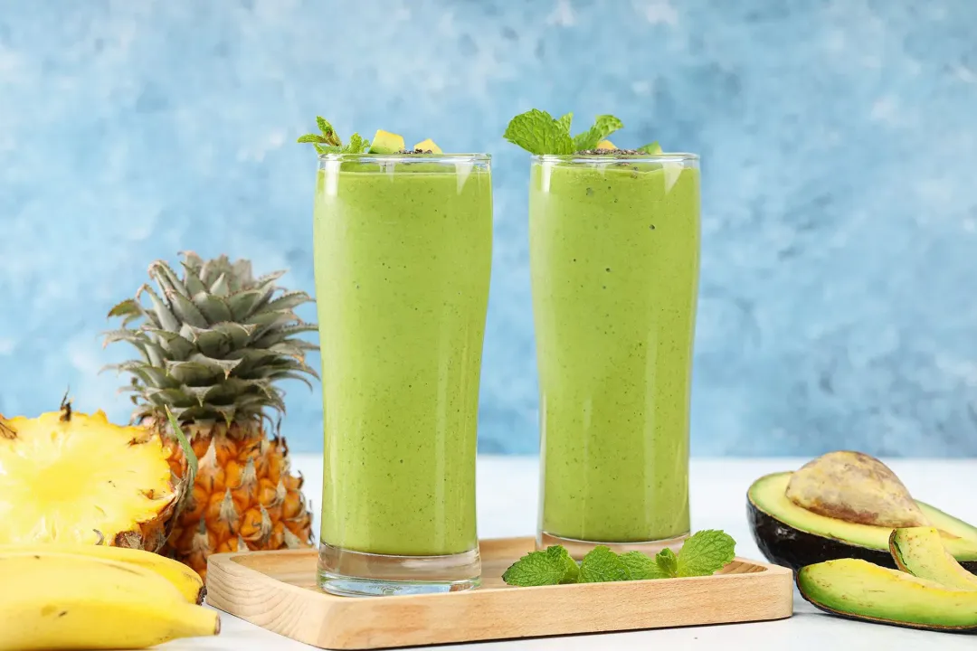 a blended avocado green smoothie poured from the blender to a glass