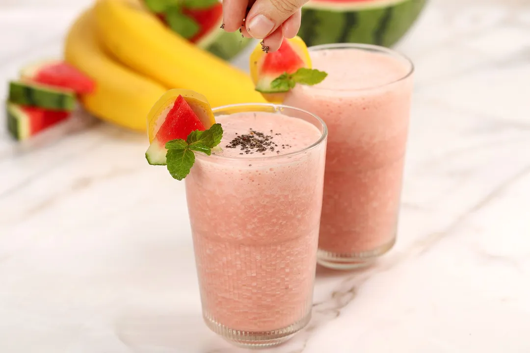 Two glasses of Watermelon Banana Smoothie placed near bananas and watermelon.