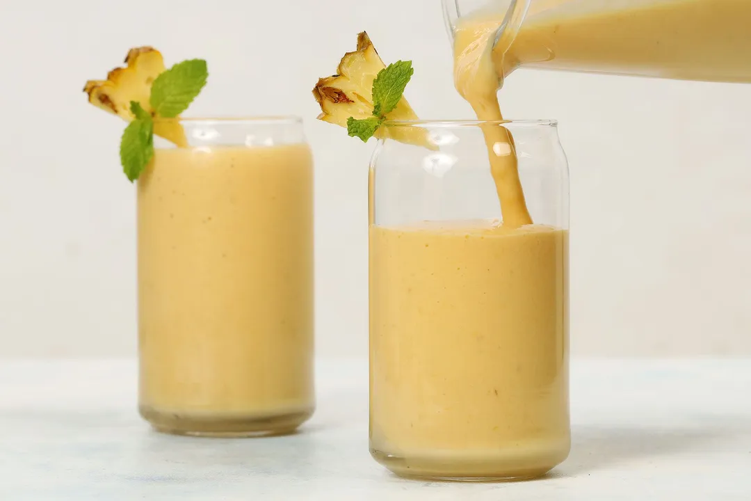 pouring yellow smoothie into two glasses