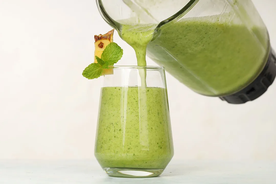 pouring green smoothie from a pitcher into glass