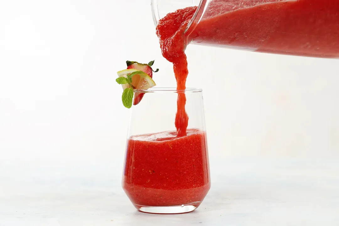 pouring red smoothie from pitcher into glass